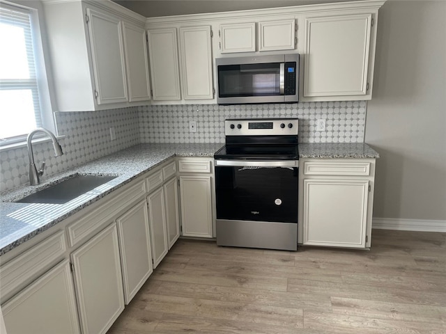 kitchen featuring white cabinets, sink, light hardwood / wood-style flooring, decorative backsplash, and appliances with stainless steel finishes