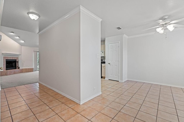 tiled spare room with crown molding, ceiling fan, and a brick fireplace