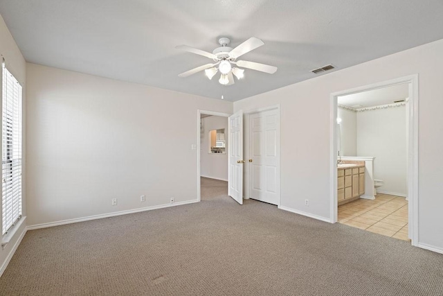 unfurnished bedroom featuring ensuite bathroom, light carpet, ceiling fan, and a closet