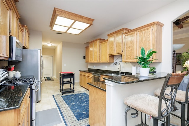 kitchen with kitchen peninsula, sink, a kitchen breakfast bar, appliances with stainless steel finishes, and dark stone countertops