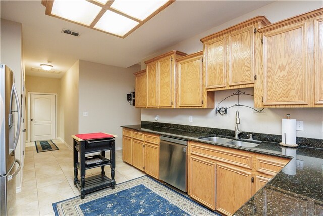 kitchen with stainless steel appliances, light tile patterned flooring, sink, dark stone counters, and light brown cabinets