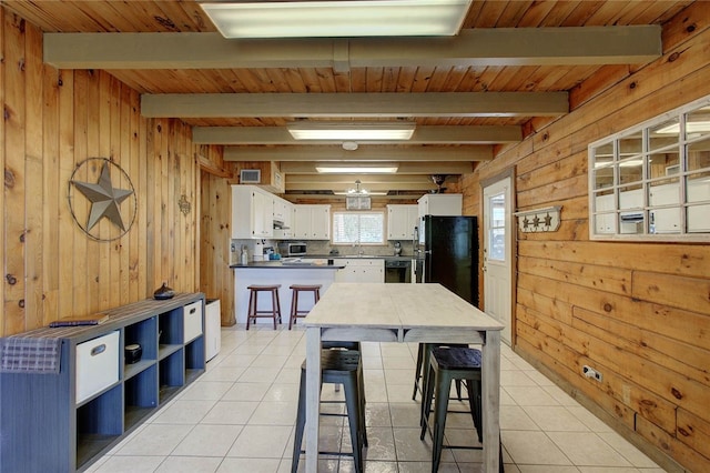 kitchen featuring black appliances, wood walls, beamed ceiling, and white cabinets