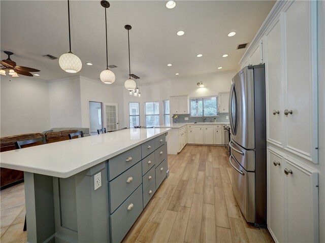 kitchen featuring light hardwood / wood-style floors, a spacious island, hanging light fixtures, stainless steel refrigerator, and white cabinetry