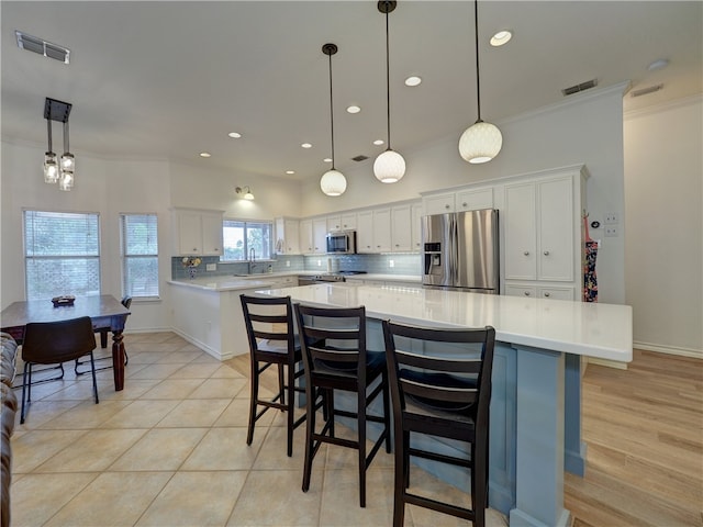 kitchen featuring stainless steel appliances, hanging light fixtures, white cabinets, and a kitchen island