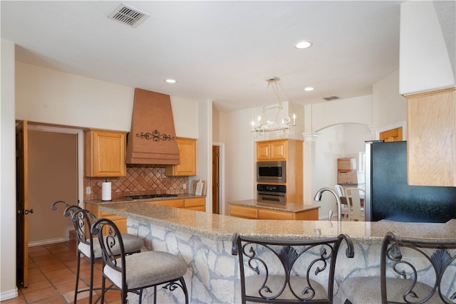 kitchen featuring premium range hood, light tile patterned flooring, kitchen peninsula, appliances with stainless steel finishes, and a chandelier