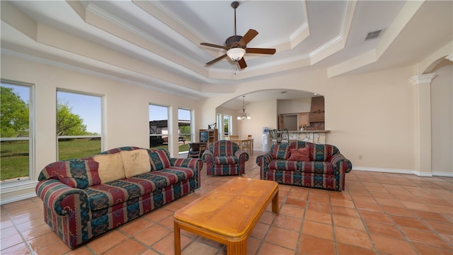 living room featuring a tray ceiling, ceiling fan with notable chandelier, light tile patterned floors, and crown molding