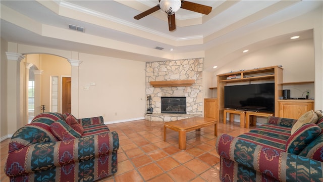 living room with crown molding, a fireplace, ornate columns, a tray ceiling, and ceiling fan