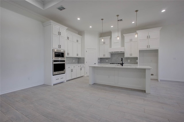 kitchen featuring light hardwood / wood-style floors, hanging light fixtures, a center island with sink, and stainless steel appliances