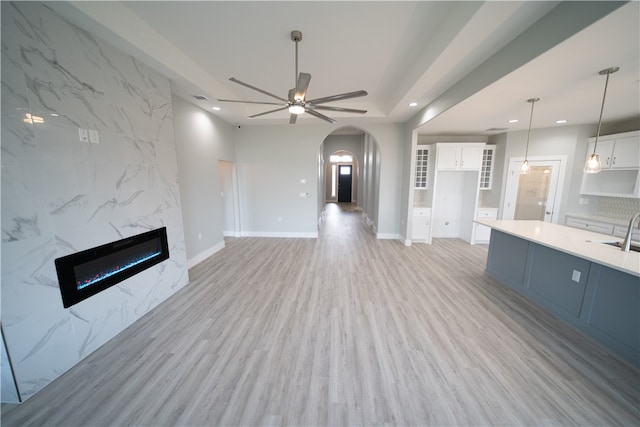 unfurnished living room with ceiling fan, light hardwood / wood-style floors, sink, and a high end fireplace