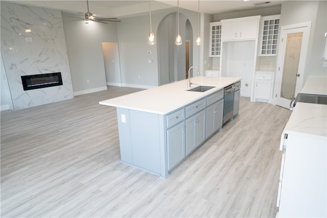 kitchen with white cabinetry, sink, light hardwood / wood-style floors, decorative light fixtures, and a kitchen island with sink