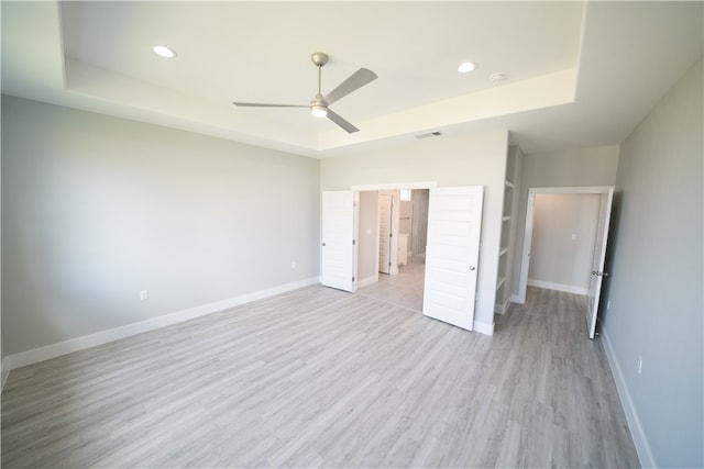 unfurnished bedroom with a raised ceiling, ensuite bath, ceiling fan, and light hardwood / wood-style floors