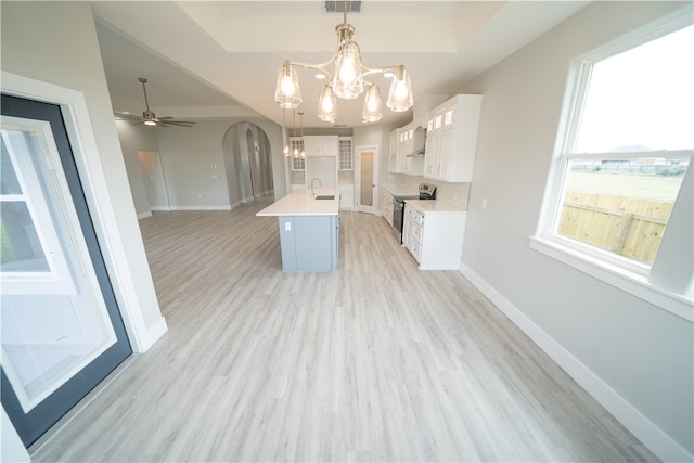 kitchen featuring a kitchen island with sink, sink, electric range, decorative light fixtures, and white cabinetry