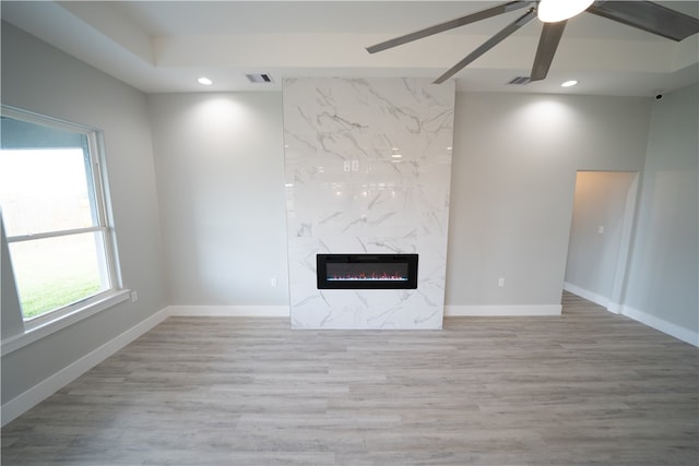 unfurnished living room featuring a wealth of natural light, ceiling fan, a premium fireplace, and light wood-type flooring