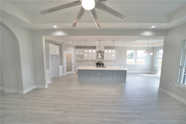 kitchen with stainless steel range, a large island with sink, light hardwood / wood-style flooring, white cabinets, and hanging light fixtures