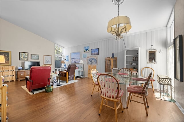 dining area with hardwood / wood-style floors, vaulted ceiling, and a notable chandelier