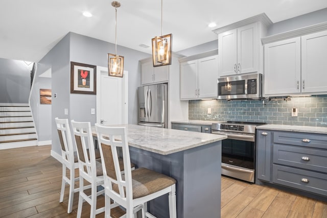 kitchen featuring stainless steel appliances, a kitchen island, light hardwood / wood-style flooring, and decorative light fixtures