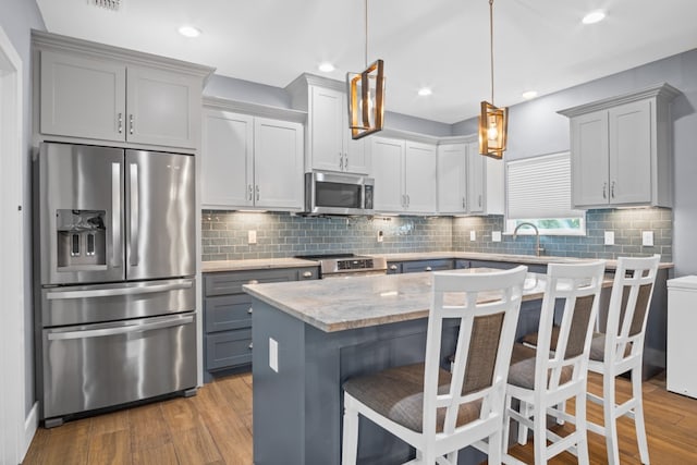 kitchen featuring a kitchen island, a breakfast bar, light wood-type flooring, appliances with stainless steel finishes, and decorative light fixtures