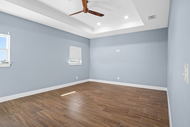 spare room with dark wood-type flooring, ceiling fan, and a raised ceiling