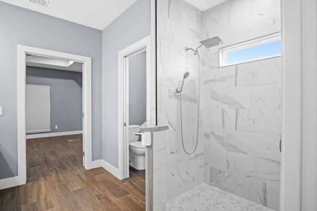 bathroom with tiled shower, hardwood / wood-style flooring, and toilet