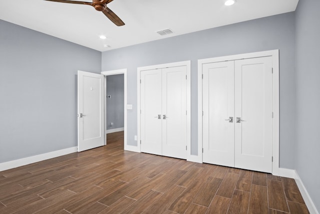 unfurnished bedroom with multiple closets, dark wood-type flooring, and ceiling fan