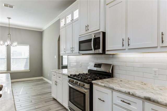 kitchen featuring white cabinets, appliances with stainless steel finishes, backsplash, glass insert cabinets, and crown molding