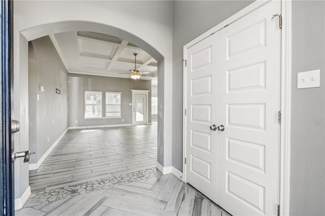 foyer entrance featuring arched walkways, beam ceiling, a ceiling fan, coffered ceiling, and baseboards