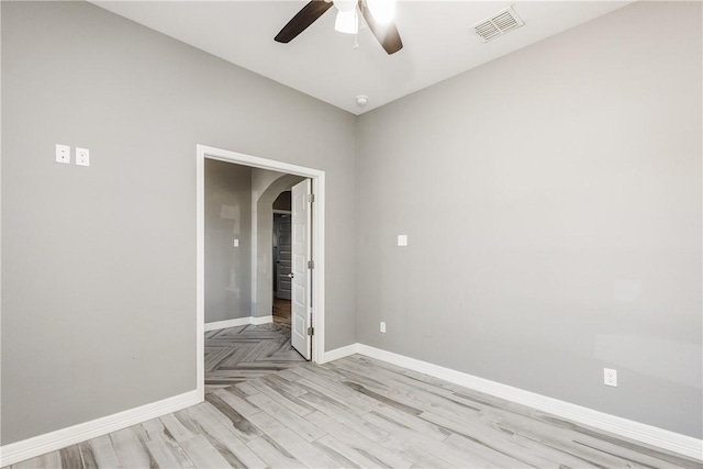 spare room featuring arched walkways, visible vents, light wood-style floors, a ceiling fan, and baseboards