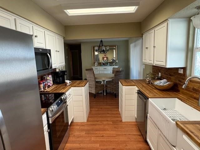 kitchen featuring butcher block countertops, appliances with stainless steel finishes, white cabinets, and a sink