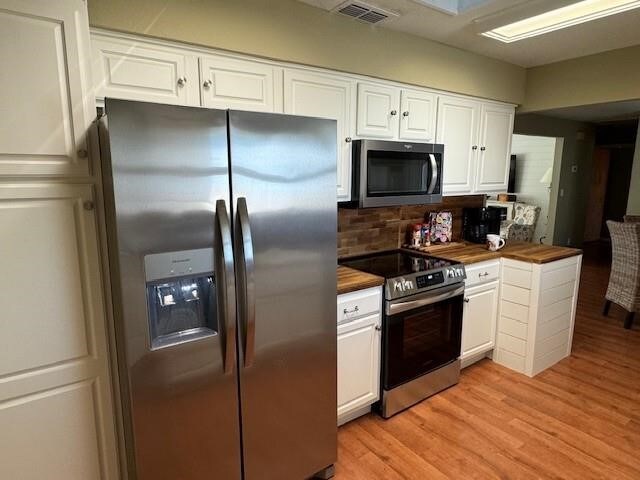 kitchen with appliances with stainless steel finishes, butcher block counters, white cabinetry, and tasteful backsplash