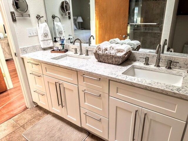 full bathroom with double vanity, a shower with door, and a sink