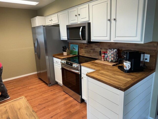 kitchen with butcher block countertops, stainless steel appliances, a sink, and white cabinetry