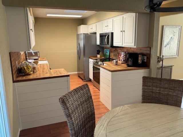 kitchen with stainless steel appliances, light wood-type flooring, decorative backsplash, butcher block countertops, and white cabinets