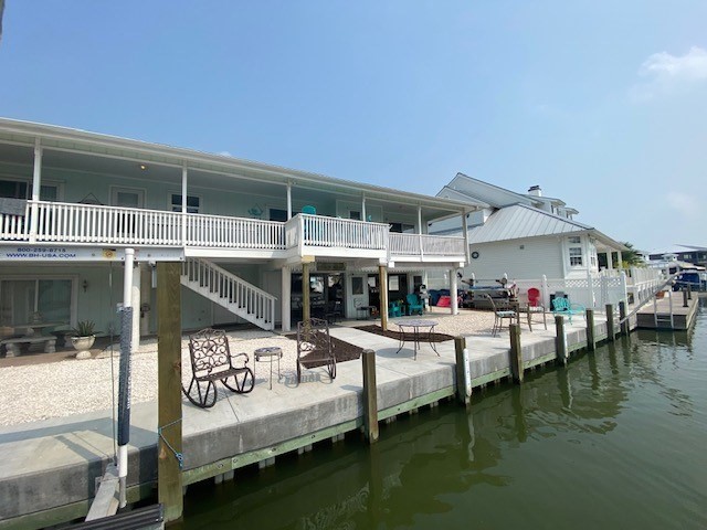 dock featuring a patio, a water view, stairway, and fence
