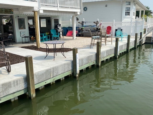 view of dock featuring a patio area, a water view, and fence