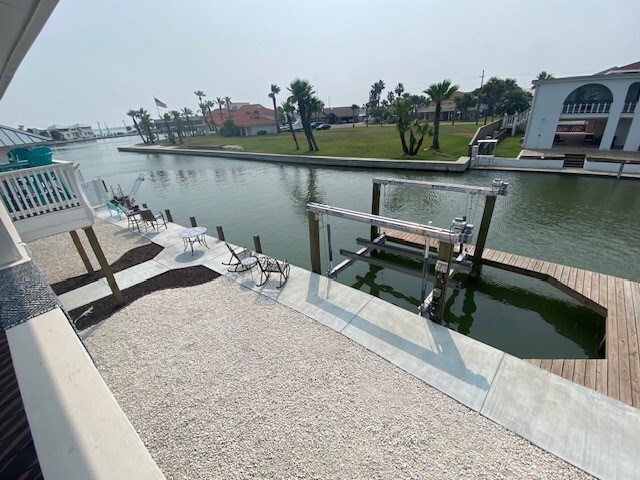dock featuring a patio, a water view, stairway, and fence