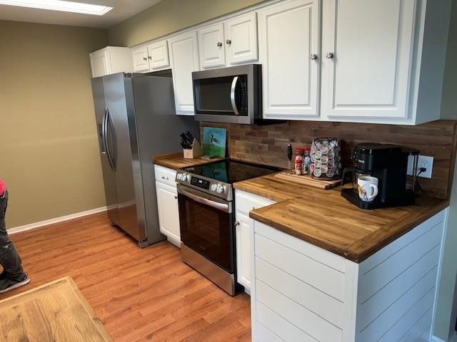 kitchen featuring wooden counters, light wood-style flooring, appliances with stainless steel finishes, white cabinets, and baseboards