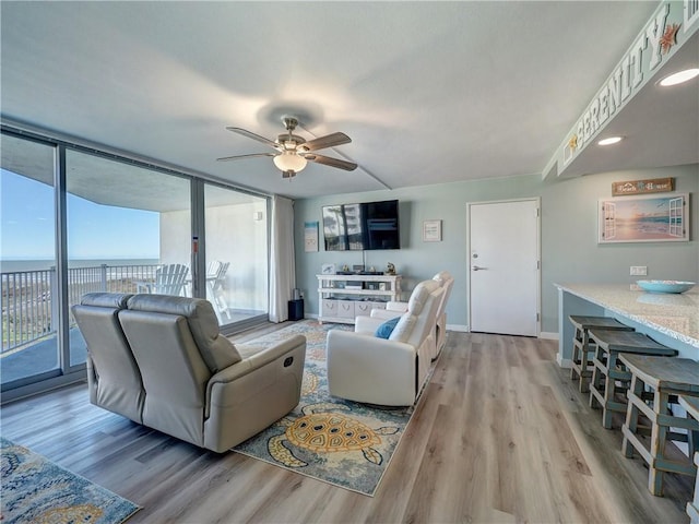 living room with a water view, expansive windows, light hardwood / wood-style floors, and ceiling fan