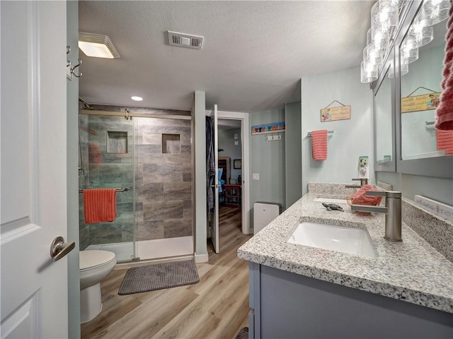 bathroom with wood-type flooring, a textured ceiling, an enclosed shower, toilet, and vanity