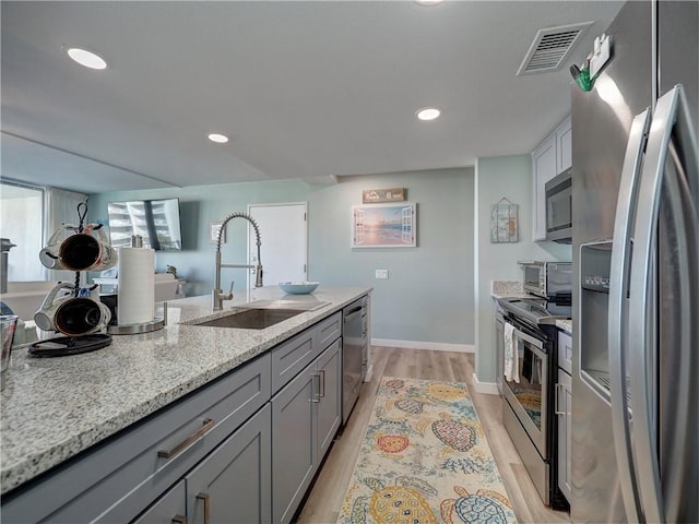 kitchen featuring gray cabinetry, sink, light wood-type flooring, appliances with stainless steel finishes, and light stone counters