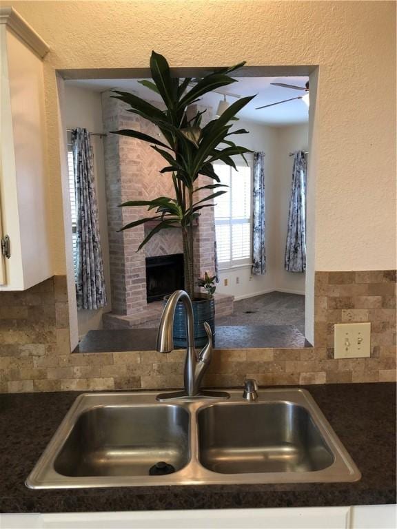 interior details with decorative backsplash, sink, white cabinets, and a fireplace