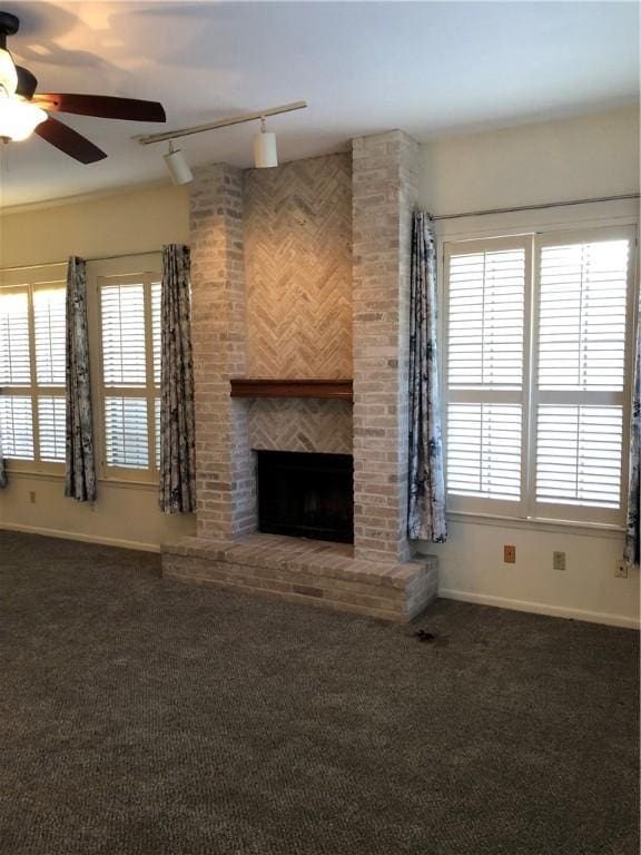 unfurnished living room featuring track lighting, ceiling fan, a brick fireplace, and dark colored carpet