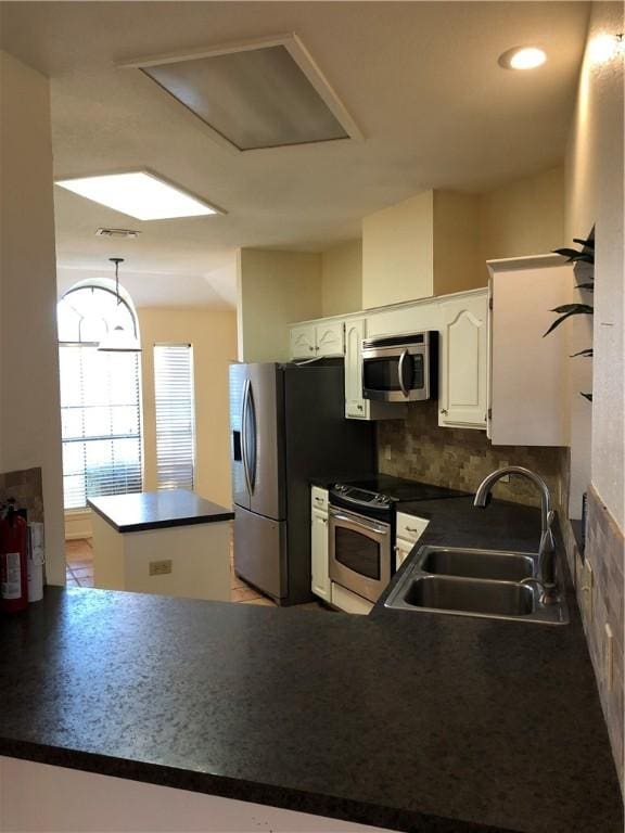 kitchen with appliances with stainless steel finishes, white cabinets, sink, kitchen peninsula, and backsplash