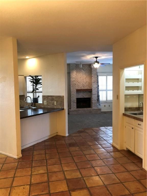 kitchen featuring dark tile patterned flooring, white cabinetry, a brick fireplace, sink, and ceiling fan