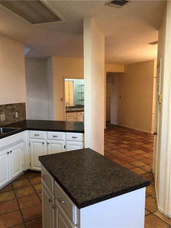 kitchen featuring sink, dark tile patterned flooring, white cabinets, and tasteful backsplash