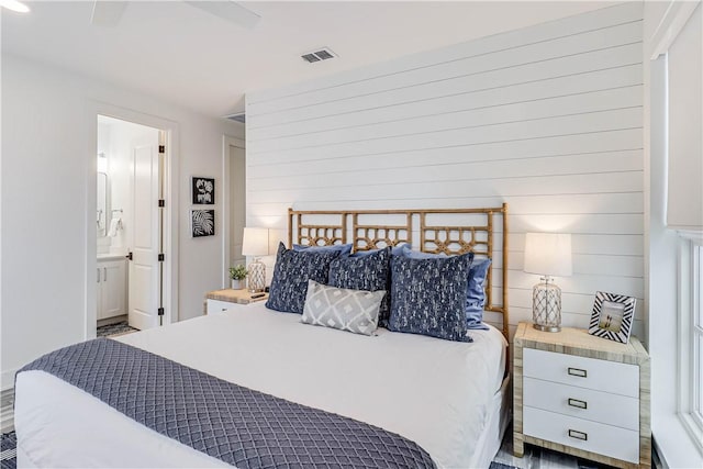 bedroom with ensuite bathroom, ceiling fan, and wood walls