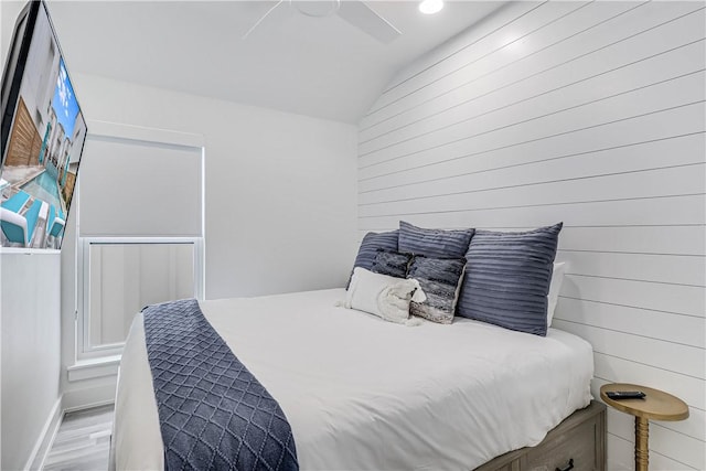 bedroom with light hardwood / wood-style flooring, ceiling fan, lofted ceiling, and wood walls