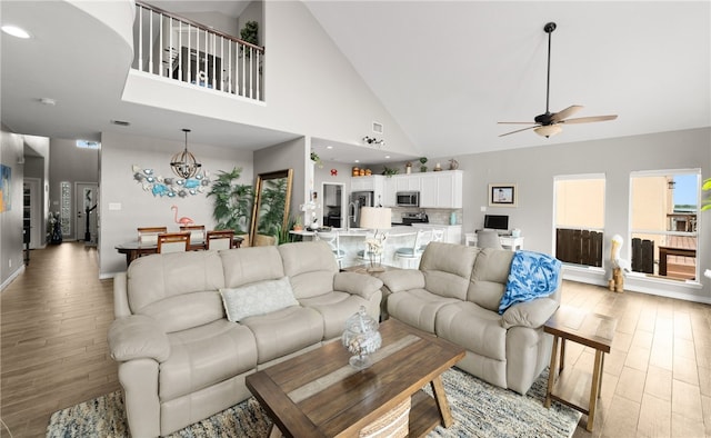 living room featuring ceiling fan with notable chandelier, light wood-type flooring, and high vaulted ceiling