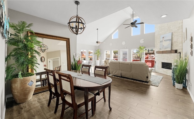 dining room featuring high vaulted ceiling, a stone fireplace, plenty of natural light, and dark wood-type flooring