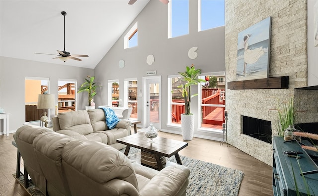 living room featuring hardwood / wood-style floors, high vaulted ceiling, ceiling fan, and a stone fireplace