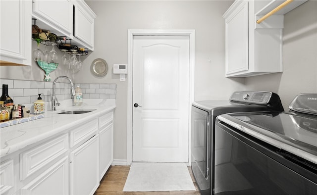 clothes washing area with washer and clothes dryer, cabinets, wood-type flooring, and wet bar